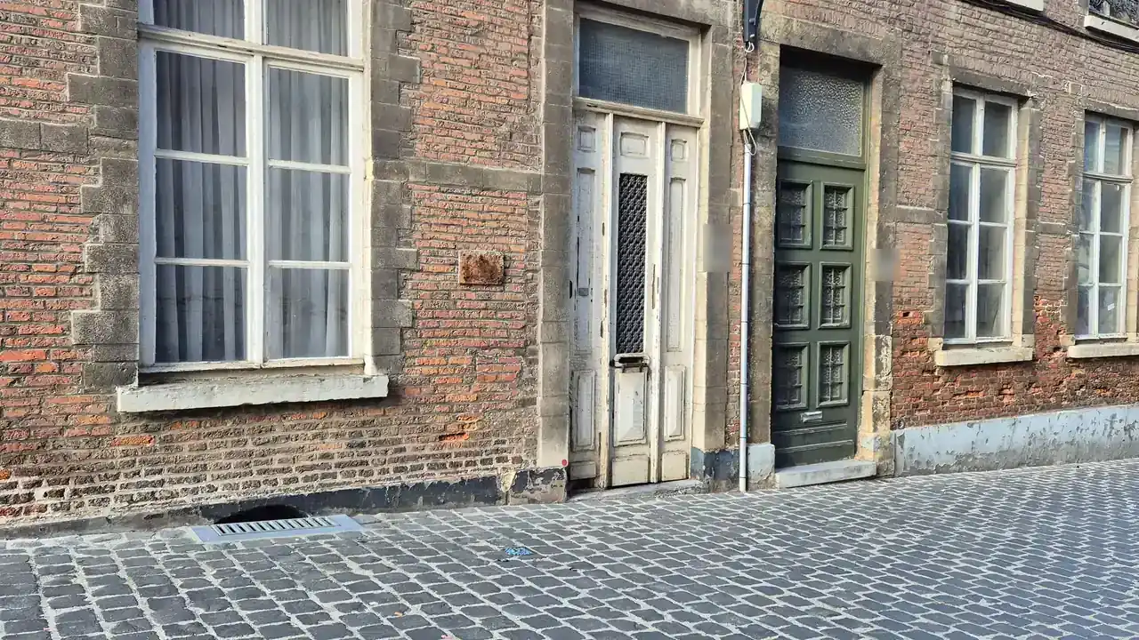 Façade en brique avec encadrements en pierre, portes anciennes et trottoir pavé