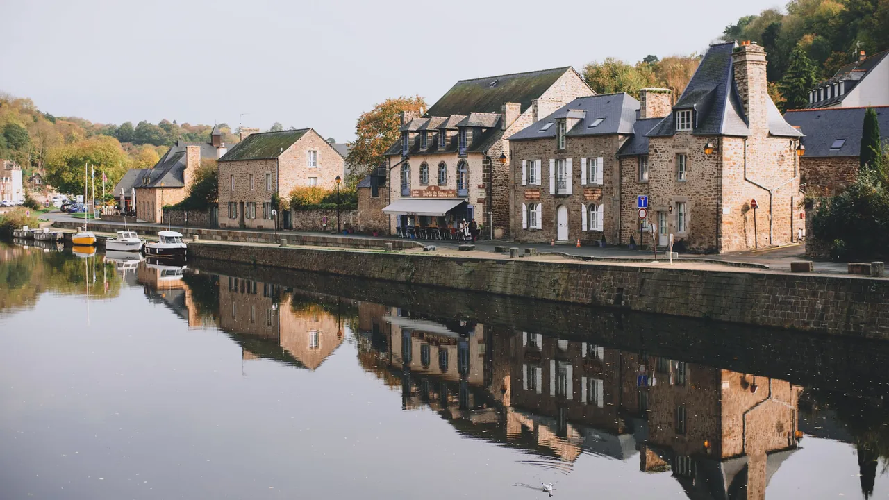Maisons anciennes en pierre et en brique le long d'un quai, reflétées dans l'eau