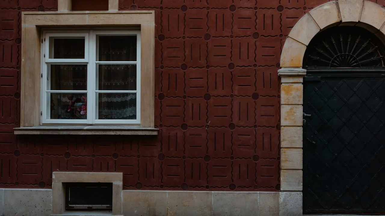Porte cintrée noire encadrée de pierre et fenêtre à châssis blanc dans une façade rouge
